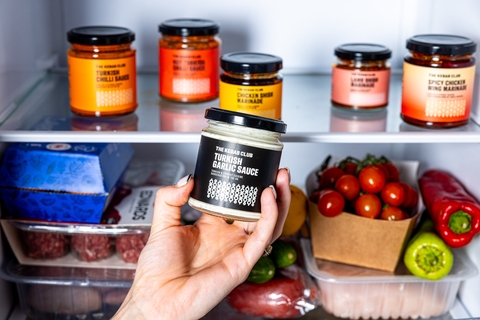 Hand holding a jar of sauce in front of shelves with various food items