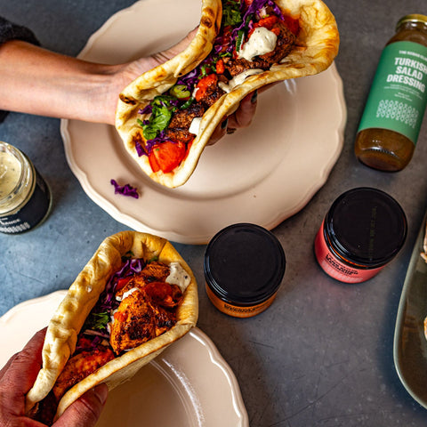 Person holding a taco with various toppings on a table with condiments and a bottle of beer.