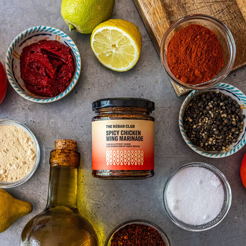 Spicy chicken wing marinade jar surrounded by spices and ingredients on a gray surface