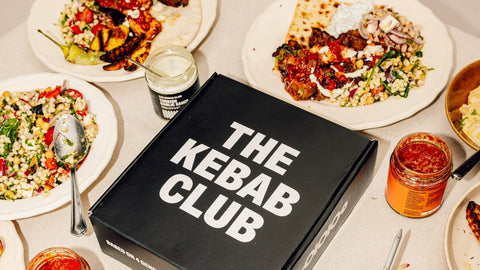 Plates of food and 'The Kebab Club' box on a table.