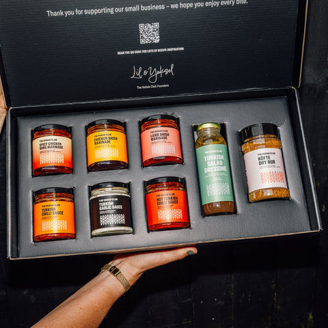 Set of candles and small bottles in a black box held by a person.