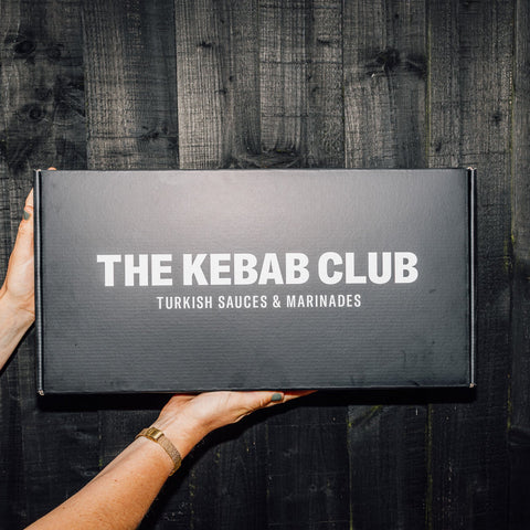 Person holding a black box with 'The Kebab Club' branding on a dark wooden background