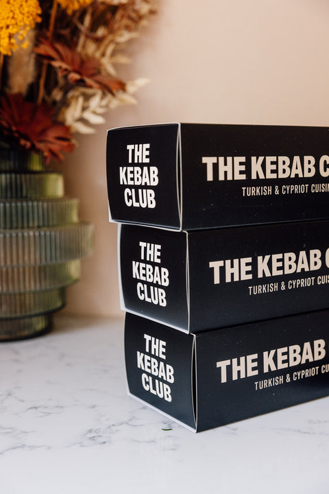Stack of black boxes with 'The Kebab Club' branding on a marble surface.